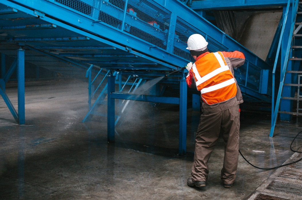 Der Arbeiter reinigt die Ausrüstung in der Müllsortieranlage. Abfallverwertungsanlage. Technologischer Prozess. Recycling und Lagerung von Abfällen zur weiteren Entsorgung.