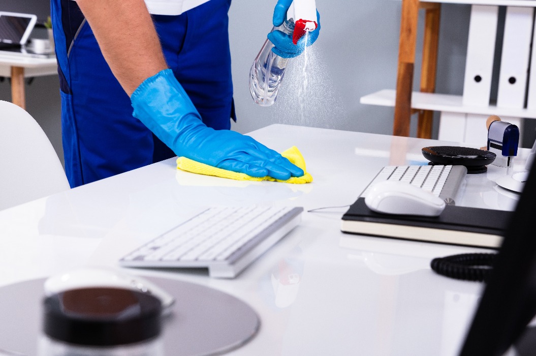 Hausmeister reinigt weißen Schreibtisch im Büro